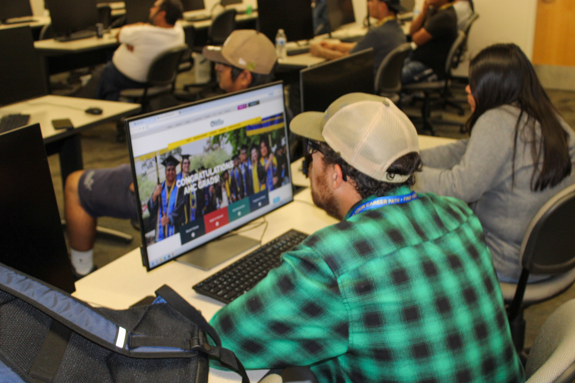 An Allan Hancock College student sits at a desktop computer in a campus computer lab, viewing the college website. Other students work at computer stations throughout the classroom, highlighting the college’s technology and academic support resources.